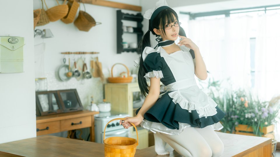 A young woman in a black and white maid cosplay outfit with glasses kneels on a wooden table holding a woven basket.